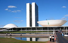 The view shows a 20th century building with two identical towers very close two each other rising from a low building which has a dome at one end, and an inverted dome, like a saucer, at the other.