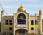 A large symmetrical two-storey building of yellow brick. The centre bay, incorporating the entrance, juts out. It has a large window with a semicircular top on the first floor and above is a golden onion dome on a blue base. At the ends of the frontage are hexagonal pilasters with small octagonal windowed pavilions and onion domes on top. Above the entrance is a white sign saying