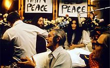 Lennon and Ono sit in front of flowers and placards bearing the word