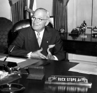 Man in suit sitting behind desk with sign that says